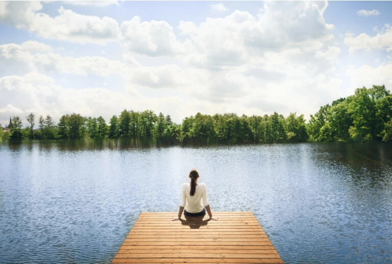 Nature has gone. Woman sitting on a wooden pier next to the lake.